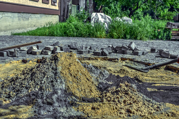 Fototapeta na wymiar The process of preparing a dry mortar for the repair of granite pavers near a private house. A pile of cement and sand on the background of a scoop shovel, paving stones and a summer landscape