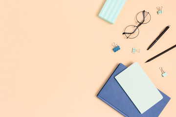 Top view of glasses, stationery, book and copybook on a beige background. Student workspace with copy space.
