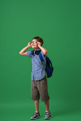 Happy cute smart boy in glasses with school bag and headphones.