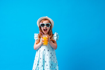 cute little girl in a dress, hat and sunglasses poses on a blue background