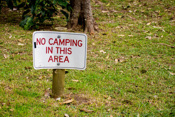 No camping in this area sign on a green grass surrounded by trees.