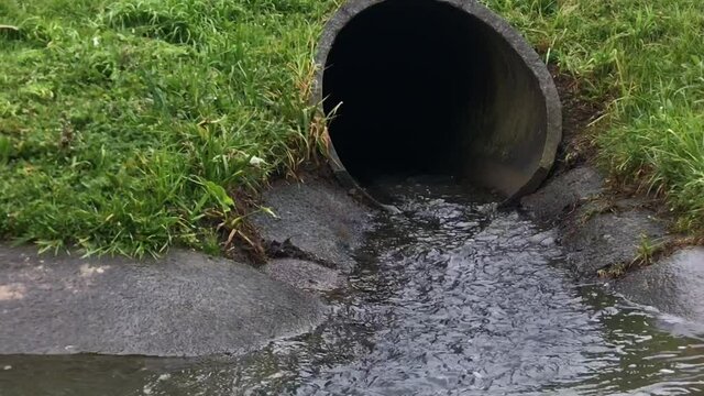 Close up view of rainwater pouring out of a storm water drain pipe into a gutter during the day in Auckland New Zealand