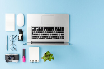 Office desktop with laptop and business accessories on blue background. Modern workspace concept. Top view