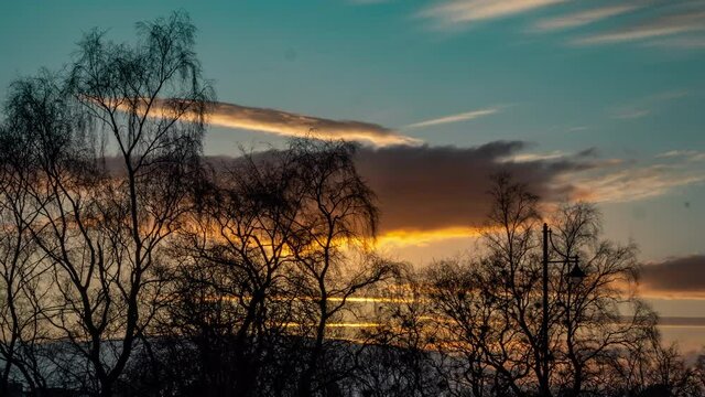 Sunset time lapse over Glasgow Scotland warm clouds over a cool sky with trees