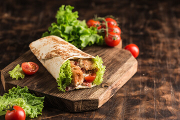 Concept of street fast food - Roll with chicken and fresh cherry tomatoes and lettuce on a wooden Board on a dark background.