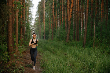 A girl in sports clothes and white Bluetooth headphones runs through the woods
