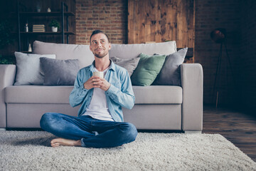 Photo of handsome homey guy sitting comfy fluffy carpet near couch drink hot fresh coffee look up...