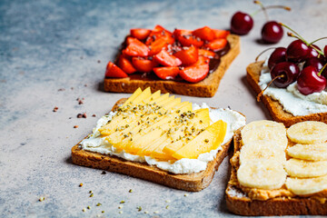 Different sweet fruit toasts with banana, mango, cherry and strawberries on dark background.