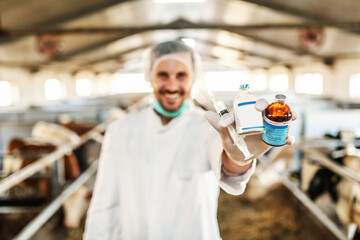 Veterinarian holding syringe and bottles with vaccine and cure for disease while standing in barn....