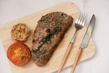Beefsteak with herb garlic and tomato on wooden cutting board with daylight concept