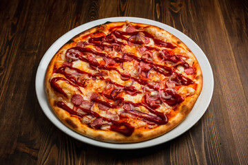 Pepperoni, bacon, sausage, onion and barbeque sauce pizza, wooden background, low key