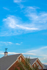 Blue sky and wispy clouds over gray gable roof with vent and weather vane