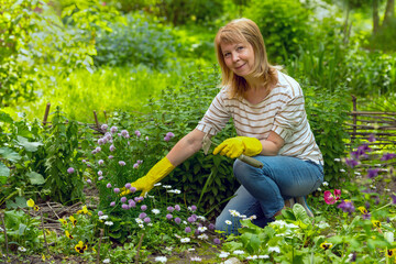 Happy mature woman with a garden tool works in her garden on a flower bed.