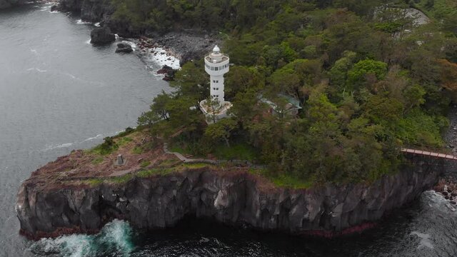 Kadowaki Lighthouse Situated On Top Of A Rocky Hill Surrounded By Green Trees With Jogasaki Coast In Ito, Shizuoka, Japan. - aerial drone