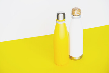 Stylish reusable eco-friendly stainless steel thermo bottles on yellow background.