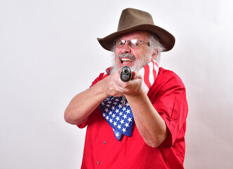 Angry old man, armed with a sawed off rifle, wearing patriotic colors, eyeglasses and a floppy western hat..Furious old man aiming his weapn right at the camera. - obrazy, fototapety, plakaty