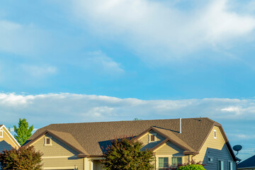 Gray roof of sunlit home with vast cloudy blue sky background on a sunny day