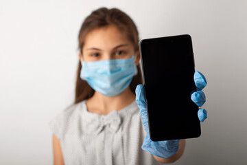 Fototapeta na wymiar Girl in dress and protective mask showing screen of the mobile phone to the camera