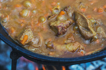 Pork soup with onions and carrots is boiling in a large cauldron. Food close-up photo. Cooking on the street while traveling.