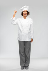 cooking, advertisement and food concept - happy smiling female chef in toque pointing finger up over grey background