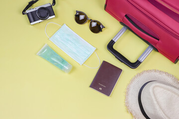 COVID-19 prevention while traveling and new normal lifestyle concept. Top view of surgical  face masks, alcohol  sanitizer gel and travel accessories on yellow background