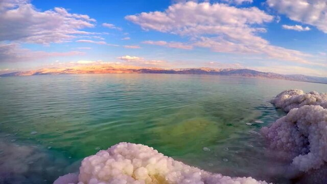Beautiful landscape of the Dead Sea, with time lapse of the water lapping against salt formations on the shore and clouds moving over the mountains of Jordan