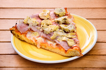 Slice of Italian pizza with ham and artichokes