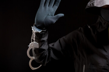 closeup of the hands of a burglar in black gloves with handcuffs on a black background