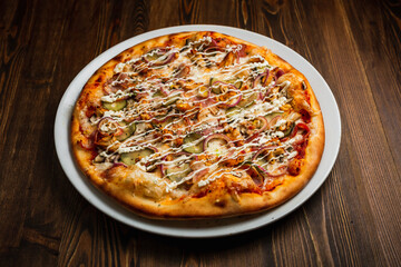 Bacon, chicken meat, mushrooms, onion, pickles and cheese pizza with mayonnaise sauce, wooden background, low key