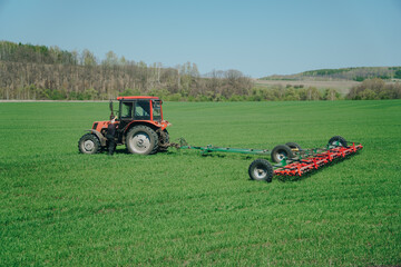 Obraz premium The tractor is working on a green spring field. Agriculture with cereal crops