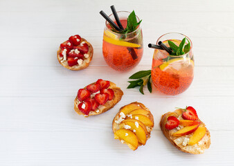 Colorful coctails and fruit toasts on white wooden table
