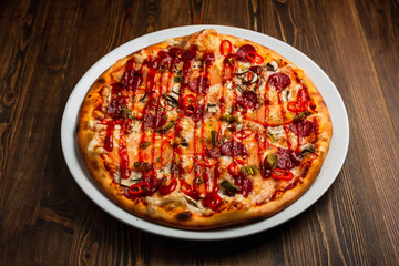 Pepperoni, mushroom, tomato, jalapeno and chili pepper and cheese spicy pizza with barbeque sauce, wooden background, low key