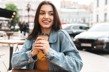 Image of woman smiling and drinking coffee while sitting at cafe