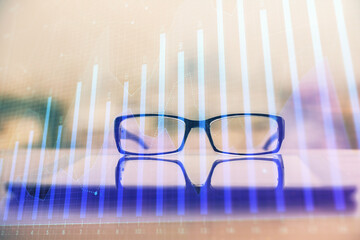 Financial graph hologram with glasses on the table background. Concept of business. Double exposure.