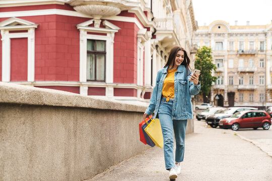 Image of happy woman using cellphone while walking with shopping bags