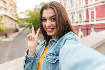 Image of woman taking selfie on cellphone and gesturing peace sign