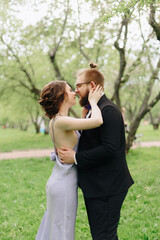 Fototapeta premium a young beautiful couple, a girl in a lilac dress and a man in black in a summer Park with Apple trees