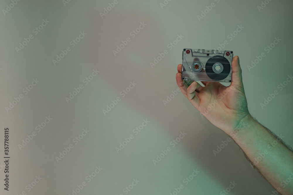 Aufkleber Hand holding audio cassette tape in the color light. Beautiful minimal in neon light. Minimalism retro style concept. Background pattern for design.