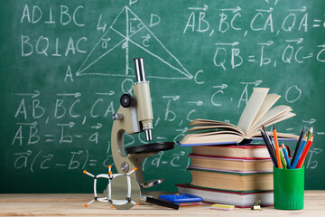 Education and sciences concept - books, molecule model and microscope on the desk in the...