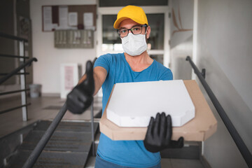 Obraz na płótnie Canvas Deliveryman with protective medical mask holding pizza box - days of viruses and pandemic, food delivery to your home.
