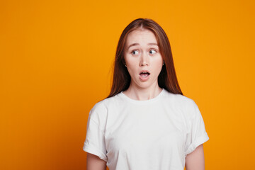 A girl with long red hair in surprise looks away with her mouth open. Portrait photo of the girl is embarrassed and surprised.
