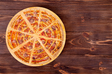 Sliced salsiccia pizza with beef sausages, mozzarella, various sauces and marinated red onions on round wood platter which is on wooden rustic background, top view and copy space