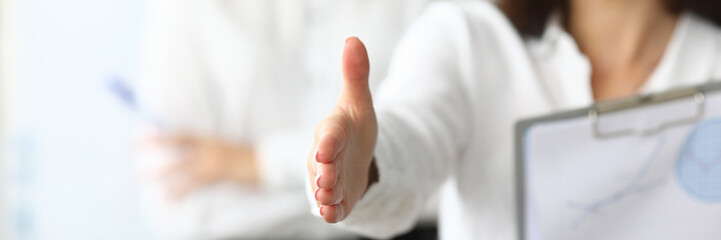 Focus on tender female hands reaching precious arm to shake hands with somebody. Joyful woman holding important paper tablet with charts and graphs. Accounting office concept. Blurred background