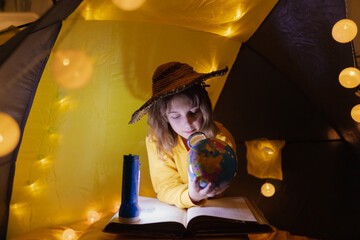 Young girl student learning and homeschooling in a home made tent with glowing light balls.