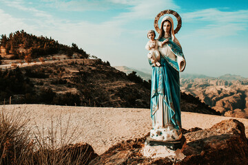 Statue of the virgin Mary in the mountains against the background of white clouds and blue sky,...