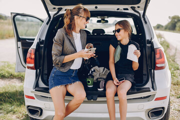 Fashionable mother with daughter. Family is sitting in the trunk. Girl in a black t-shirt. Ladies...