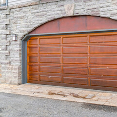 Square Arched brown wood panel garage door of home with stone brick exterior wall