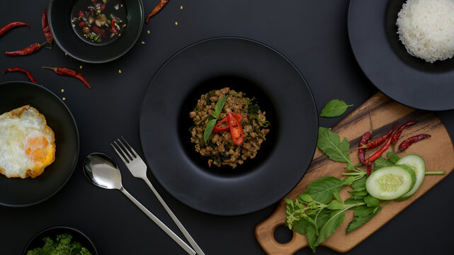 Thai traditional food, Stir fried minced pork with basil (Pad ka prao), rice fried egg serving on black ceramic plate and silverware