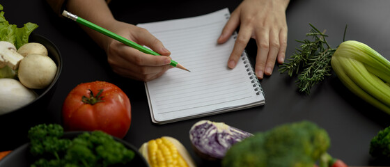Female student taking recipe notes on blank notebook on black kitchen table in cooking class
