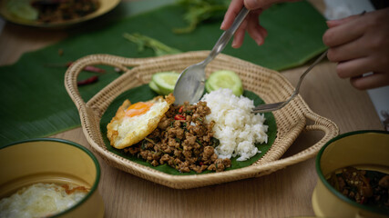 Hands holding silverware eating Thai traditional food, Stir fried minced pork with basil (Pad ka prao), rice fried egg serving on wicker plate